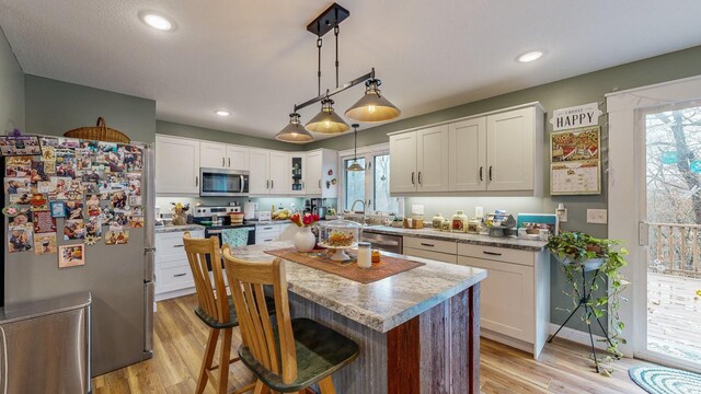 kitchen featuring stainless steel appliances, white cabinets, plenty of natural light, and light wood finished floors