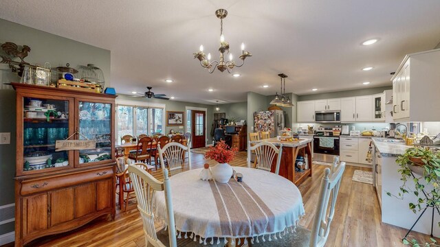 dining space with ceiling fan with notable chandelier, light wood-type flooring, and recessed lighting