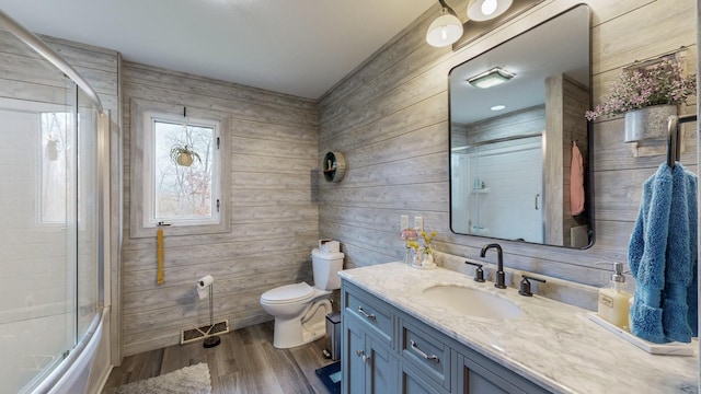 bathroom with toilet, wood finished floors, visible vents, vanity, and combined bath / shower with glass door