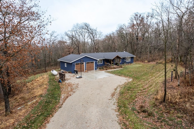 ranch-style house featuring driveway, an attached garage, a wooded view, and a front yard