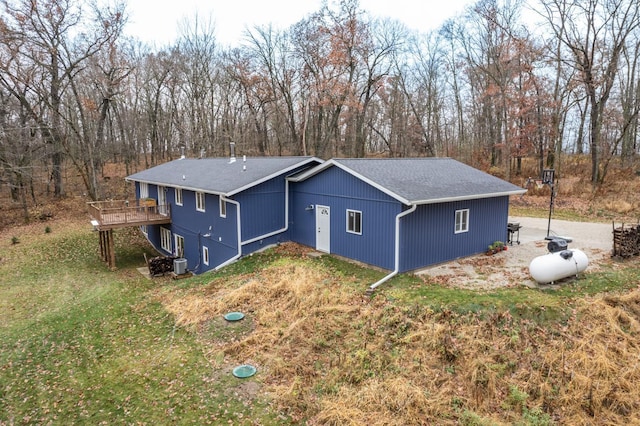 exterior space with central air condition unit, a deck, a lawn, and roof with shingles