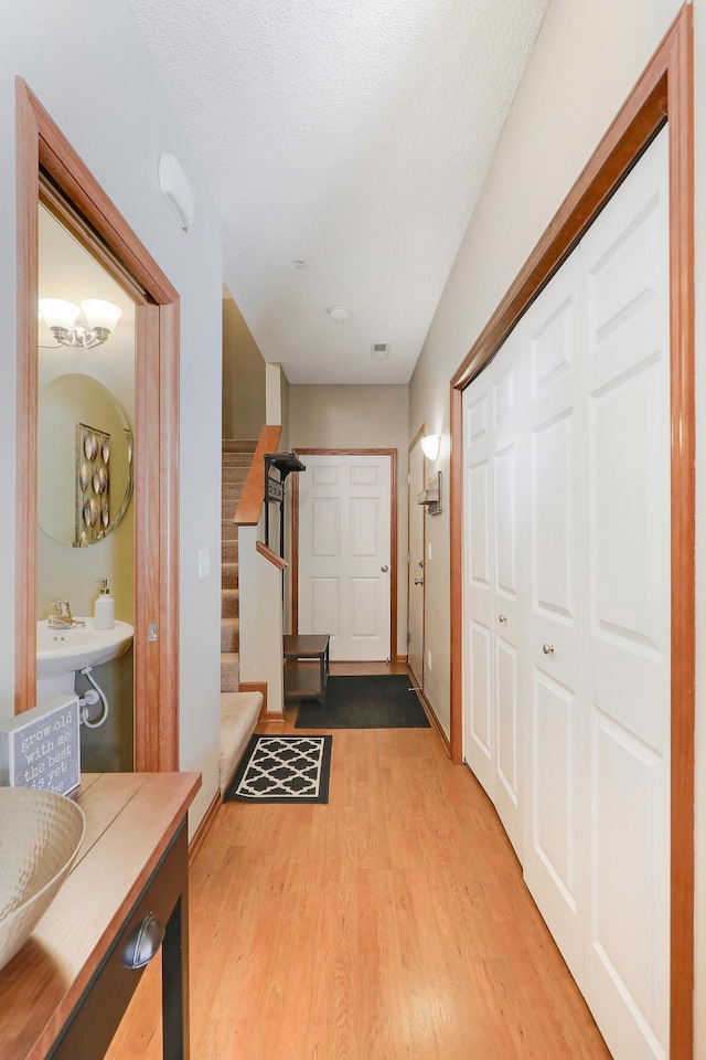 hallway with wood finished floors, visible vents, a textured ceiling, and stairs