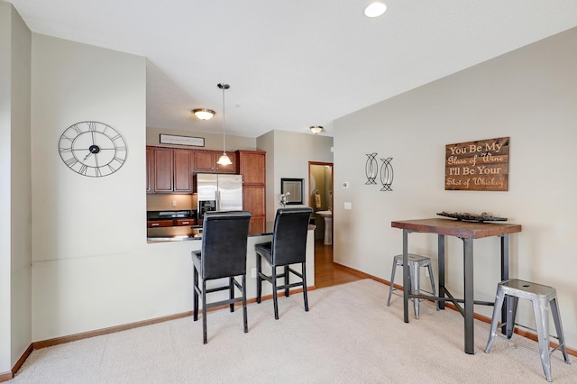 kitchen with decorative light fixtures, a breakfast bar area, light carpet, a peninsula, and stainless steel fridge with ice dispenser