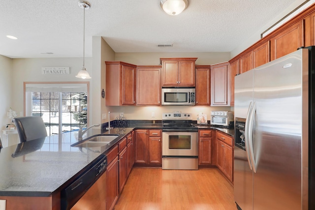 kitchen with visible vents, brown cabinetry, light wood-style flooring, appliances with stainless steel finishes, and a sink