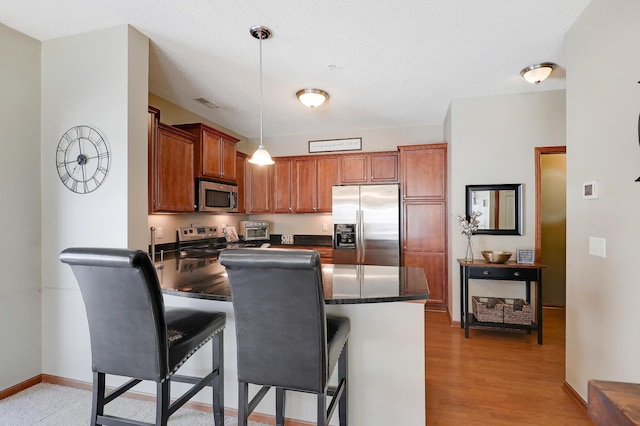 kitchen featuring decorative light fixtures, stainless steel appliances, dark countertops, a peninsula, and a kitchen breakfast bar