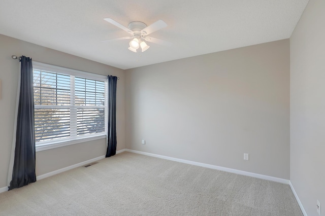 spare room with light carpet, a ceiling fan, visible vents, and baseboards