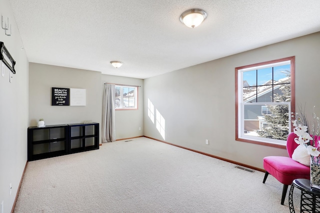 living area with visible vents, carpet flooring, a textured ceiling, and baseboards