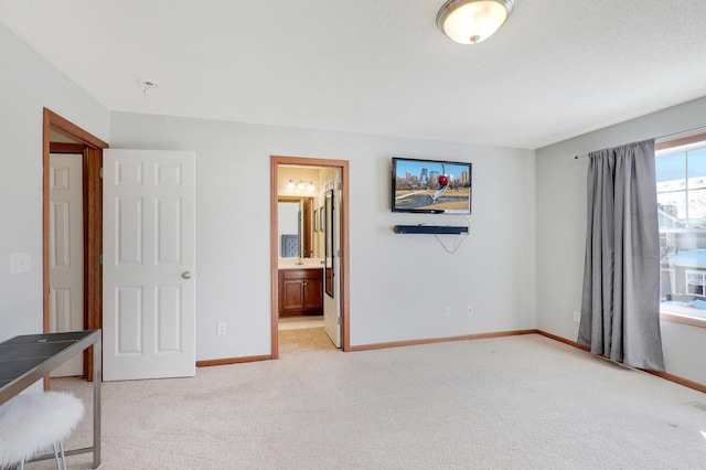 unfurnished bedroom featuring light carpet, baseboards, and ensuite bathroom