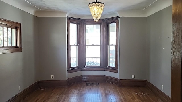 spare room featuring baseboards, hardwood / wood-style floors, visible vents, and an inviting chandelier