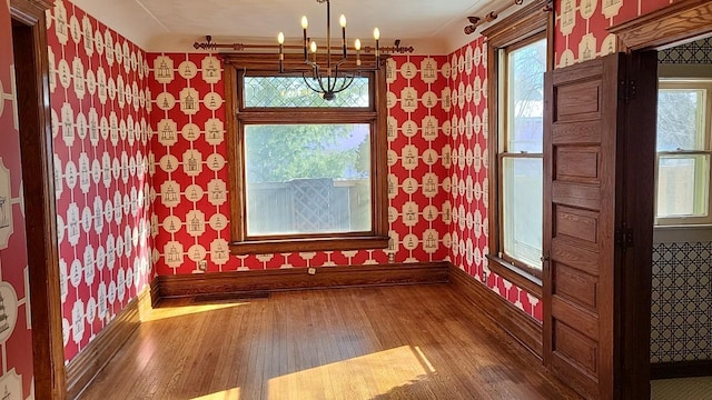 unfurnished dining area with wallpapered walls, a healthy amount of sunlight, wood finished floors, and baseboards