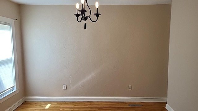 unfurnished room with baseboards, wood finished floors, and a notable chandelier