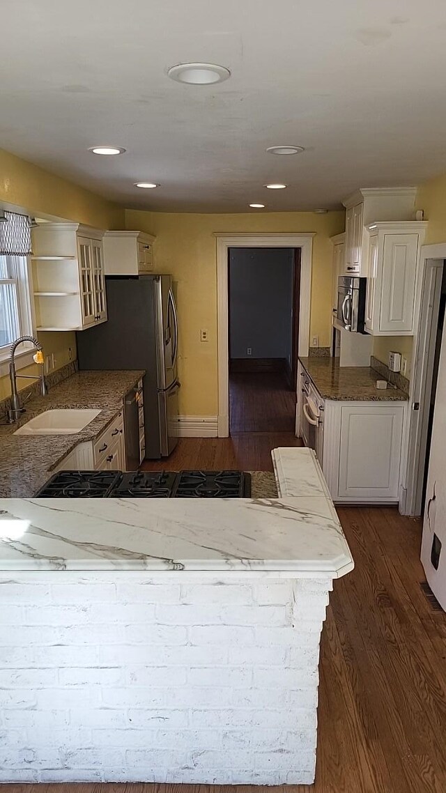 kitchen with dark wood finished floors, appliances with stainless steel finishes, white cabinetry, a sink, and dark stone counters