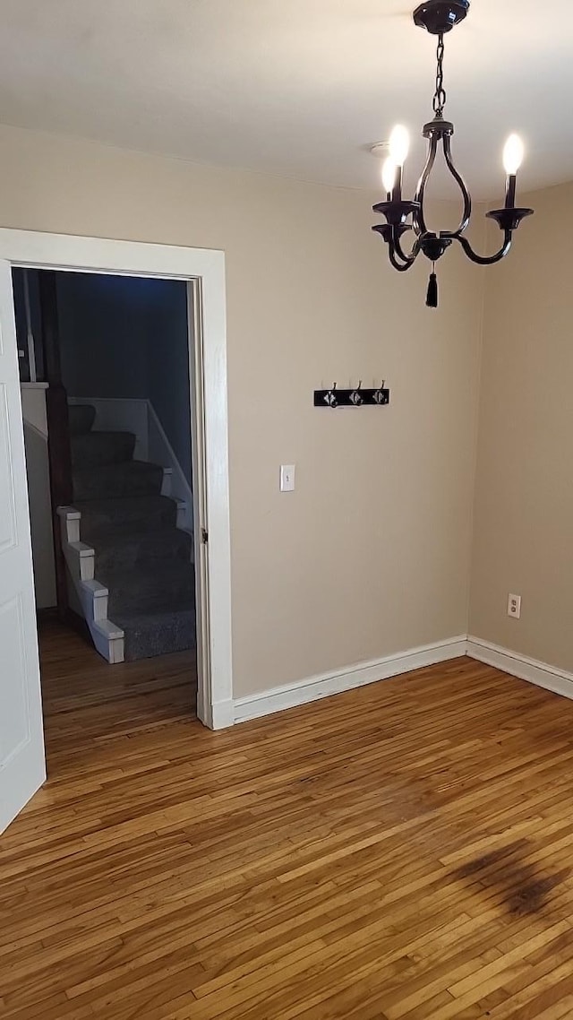 spare room featuring stairs, a notable chandelier, baseboards, and wood finished floors