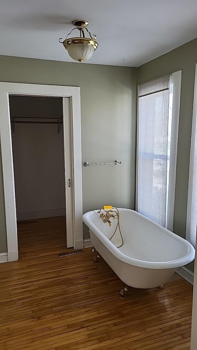 bathroom featuring a soaking tub, baseboards, and wood finished floors