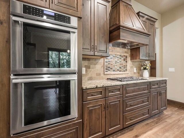 4350 Golfview Dr, Jordan, MN 55352 - kitchen featuring appliances with stainless steel finishes, wall chimney range hood, light wood-type flooring, backsplash, and light stone countertops