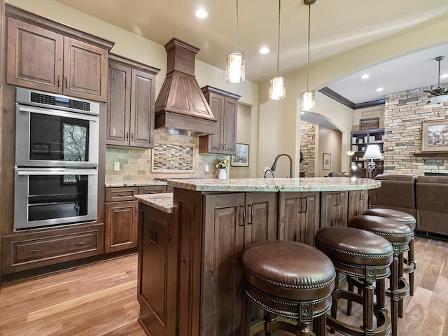 4350 Golfview Dr, Jordan, MN 55352 - kitchen with premium range hood, double oven, arched walkways, open floor plan, and light wood-style flooring