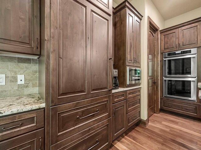 4350 Golfview Dr, Jordan, MN 55352 - kitchen featuring stainless steel double oven, tasteful backsplash, light wood-type flooring, light stone countertops, and dark brown cabinets