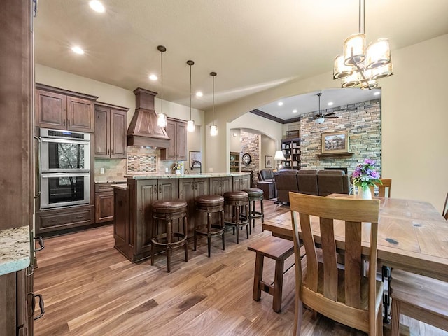 4350 Golfview Dr, Jordan, MN 55352 - kitchen with custom range hood, arched walkways, stainless steel double oven, light wood-type flooring, and backsplash
