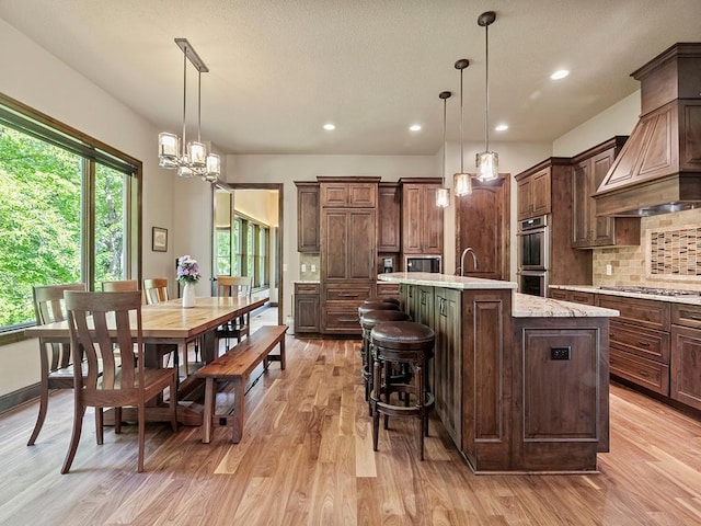 4350 Golfview Dr, Jordan, MN 55352 - kitchen with a kitchen island with sink, light wood-style flooring, premium range hood, backsplash, and appliances with stainless steel finishes