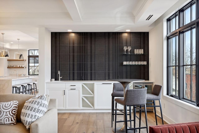 bar featuring light wood finished floors, an accent wall, baseboards, and a sink