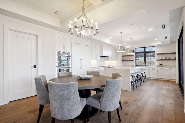 dining area with an inviting chandelier, a tray ceiling, crown molding, light wood-type flooring, and recessed lighting