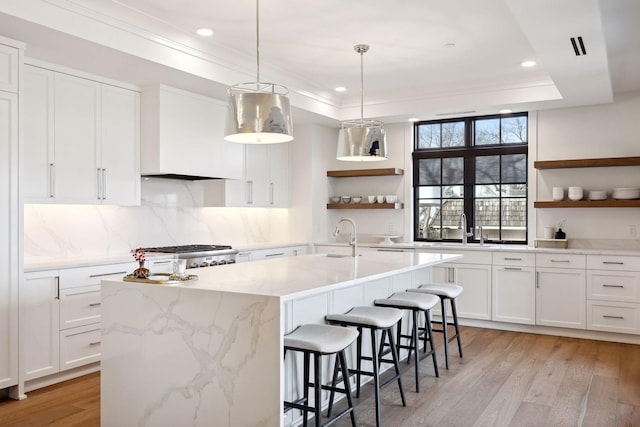 kitchen with a center island with sink, range, a tray ceiling, light wood-type flooring, and open shelves