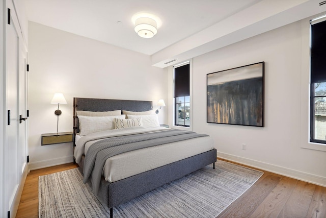 bedroom with light wood finished floors, visible vents, and baseboards