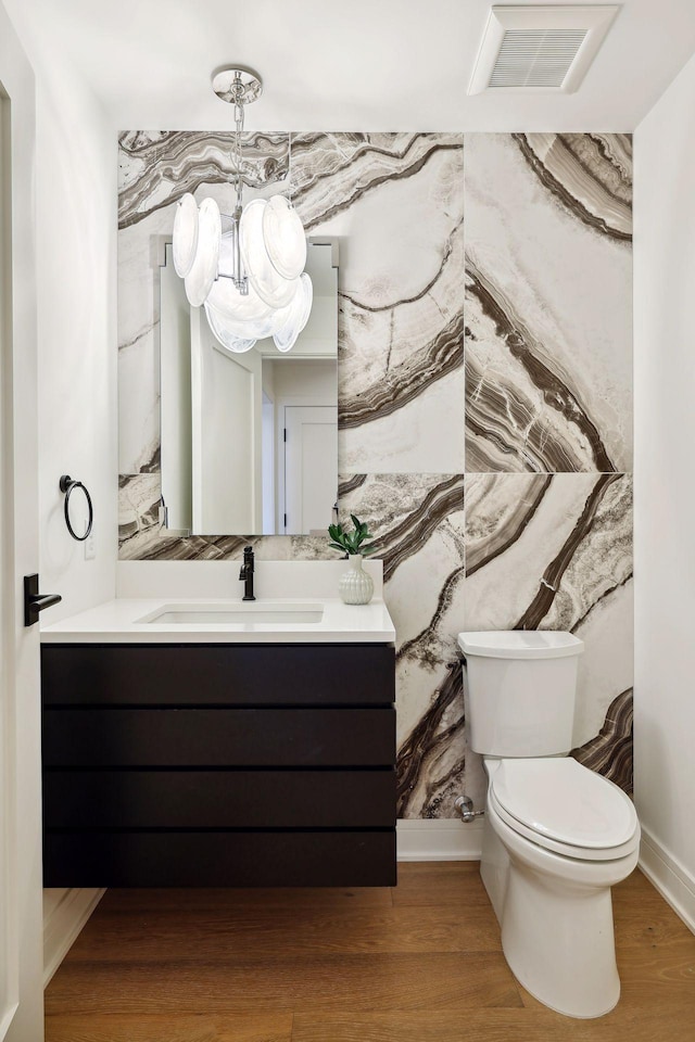 bathroom with visible vents, toilet, vanity, wood finished floors, and a chandelier