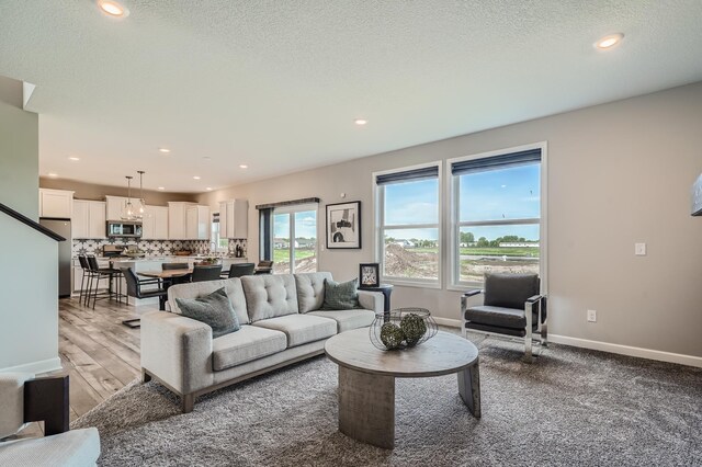 living area featuring light wood-type flooring, recessed lighting, a textured ceiling, and baseboards