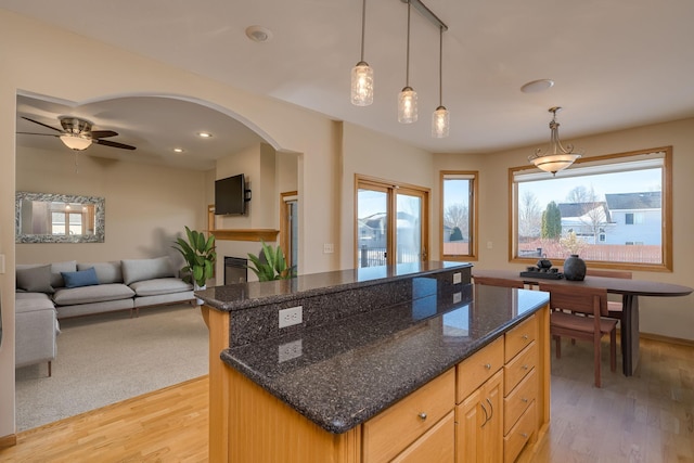 kitchen featuring a healthy amount of sunlight, light wood-style floors, arched walkways, and a center island