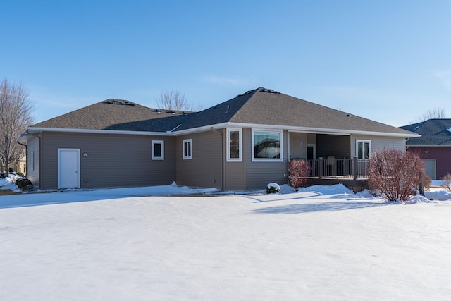 snow covered rear of property with roof with shingles