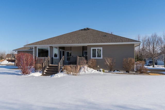 snow covered back of property featuring covered porch and a shingled roof