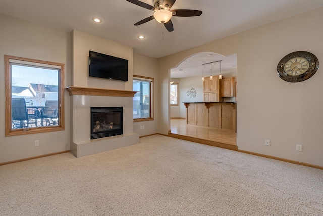 unfurnished living room with baseboards, a ceiling fan, a glass covered fireplace, light colored carpet, and recessed lighting