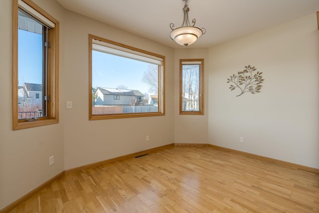 spare room featuring light wood-type flooring, visible vents, and baseboards