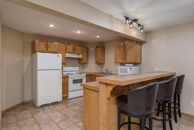 kitchen with a breakfast bar, a sink, a peninsula, white appliances, and under cabinet range hood