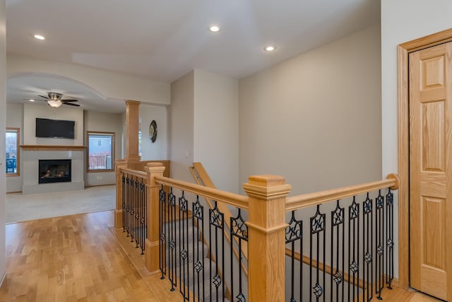 corridor with arched walkways, recessed lighting, light wood-style flooring, an upstairs landing, and ornate columns