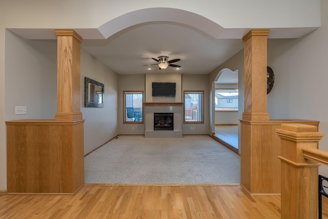 unfurnished living room with light colored carpet, decorative columns, light wood finished floors, and ceiling fan