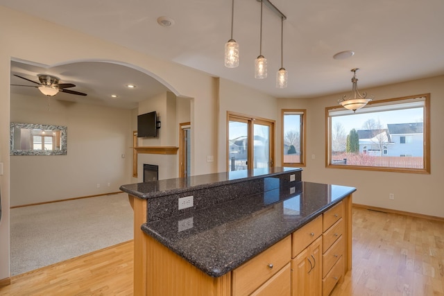 kitchen with arched walkways, a kitchen island, light wood-style flooring, and baseboards