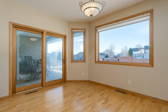 empty room with light wood-style flooring, visible vents, and baseboards