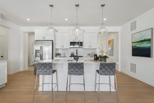 kitchen with stainless steel appliances, tasteful backsplash, a kitchen bar, and light wood-style flooring