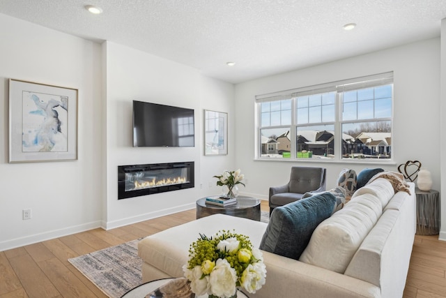 living area with wood-type flooring, baseboards, a textured ceiling, and a glass covered fireplace