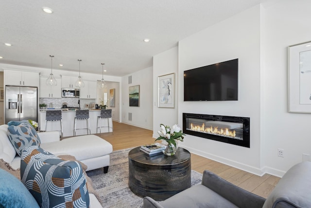 living room featuring light wood finished floors, recessed lighting, a glass covered fireplace, and baseboards