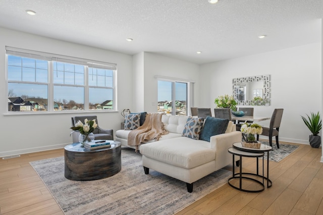 living area featuring a textured ceiling, light wood finished floors, visible vents, and baseboards