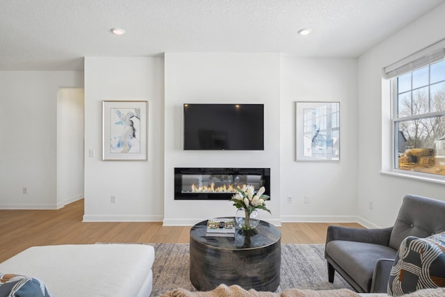 living area featuring a textured ceiling, baseboards, wood finished floors, and a glass covered fireplace