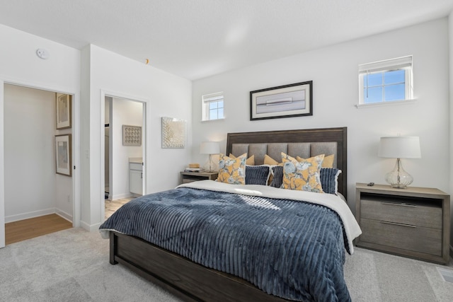 bedroom with baseboards, connected bathroom, and light colored carpet