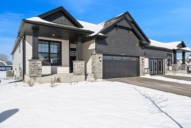 craftsman house with a garage, stone siding, central AC unit, and covered porch