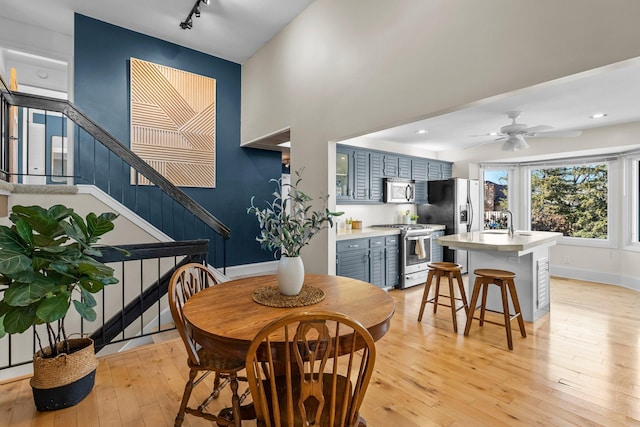 dining area featuring light wood-style flooring, rail lighting, a ceiling fan, and baseboards