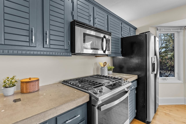 kitchen featuring light wood finished floors, appliances with stainless steel finishes, light countertops, and baseboards