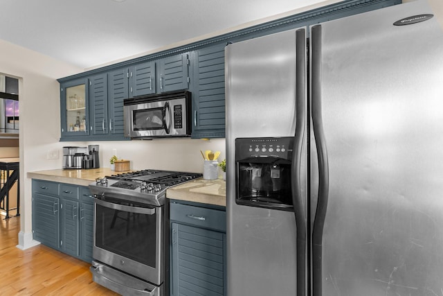 kitchen with glass insert cabinets, appliances with stainless steel finishes, light countertops, and light wood finished floors