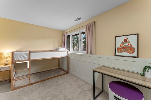 unfurnished bedroom featuring visible vents, light carpet, wainscoting, and a decorative wall